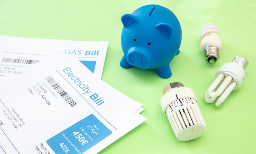 Boleta de luz y gas, hucha con forma de cerdo azul, bombillas y termostato de calefacción sobre fondo verde
